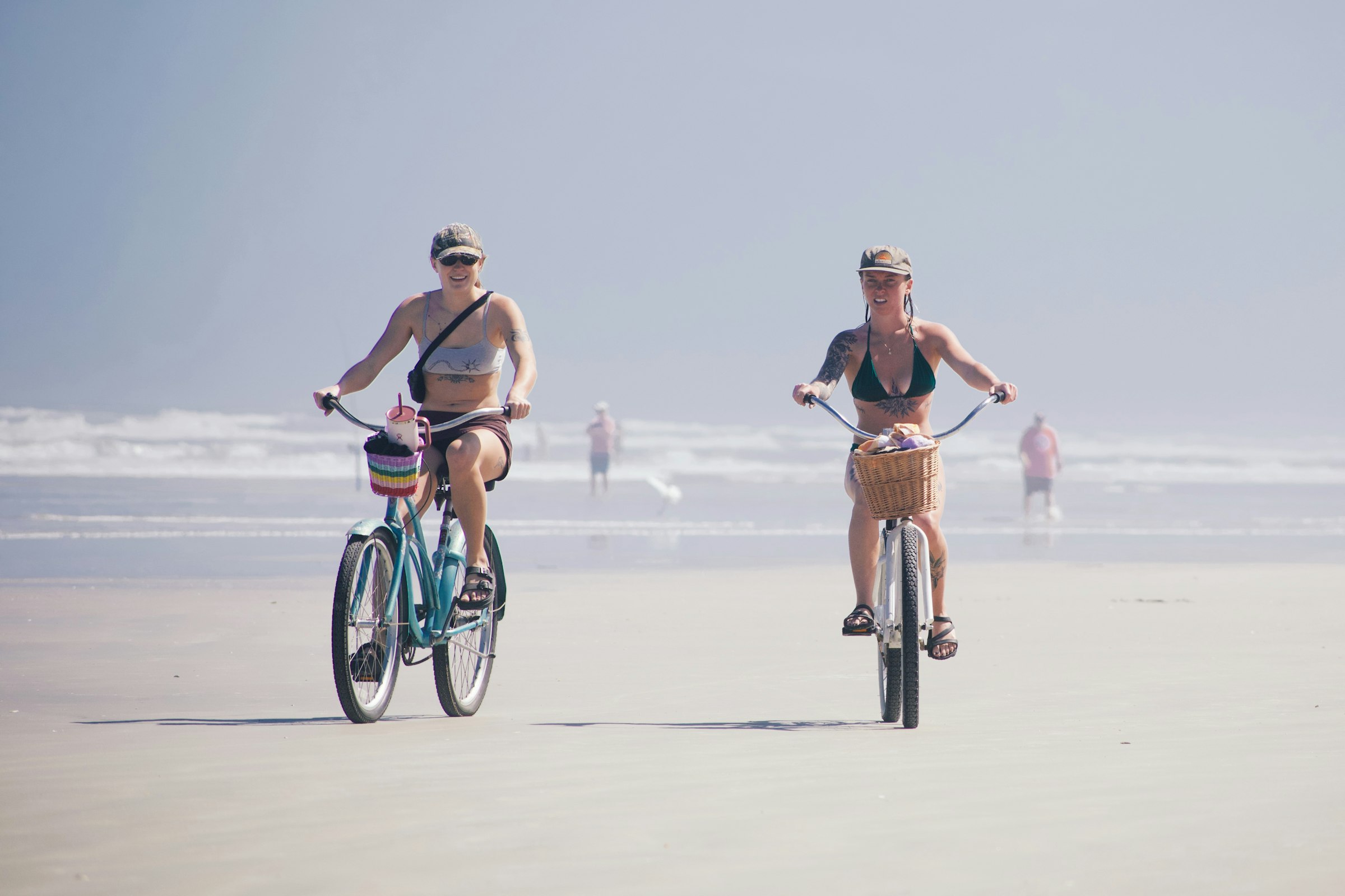 Two women riding bicycles on a sandy beach