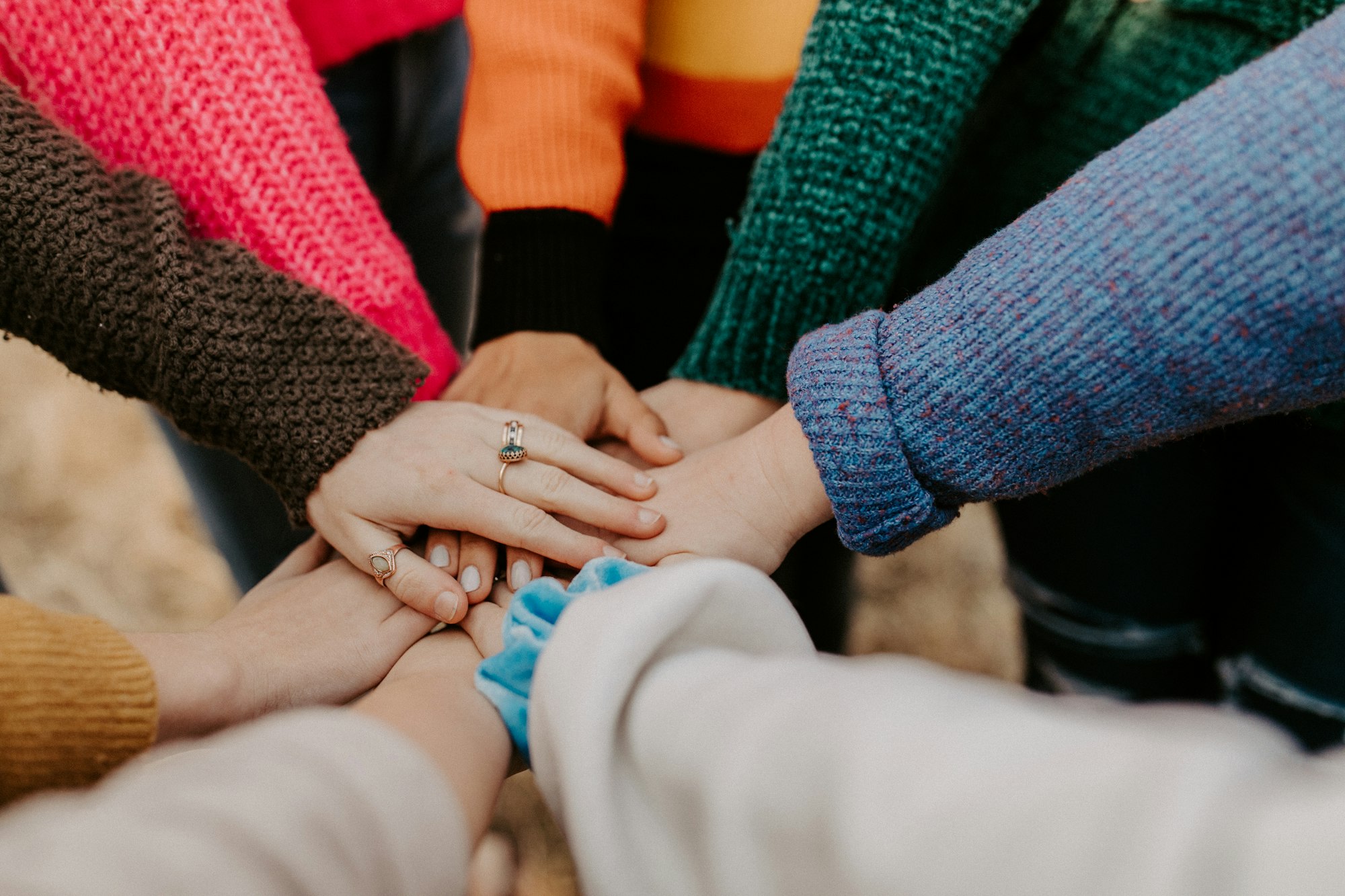A group of people in warm sweaters stacking their hands together in support